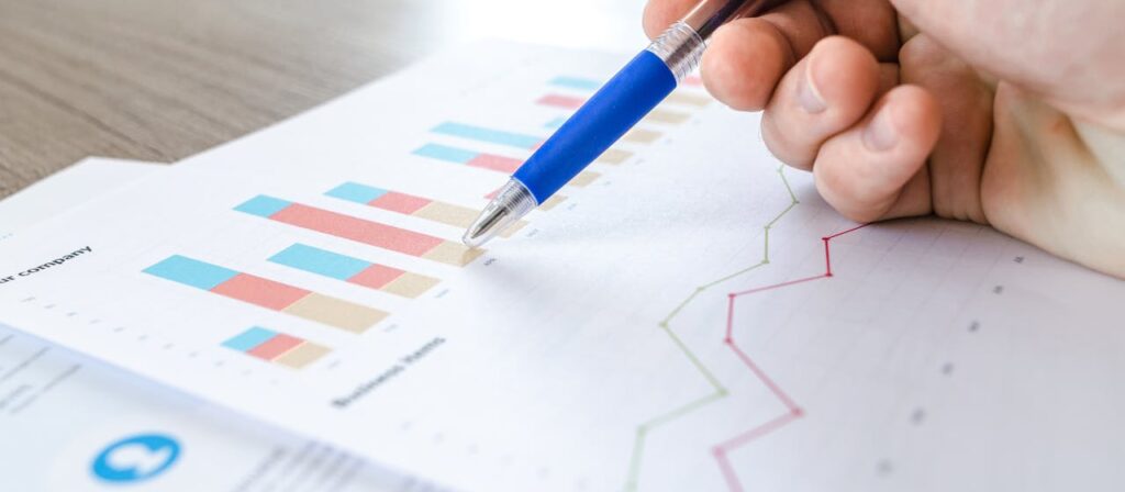 zipwp image 590022 A close-up of a hand with a pen analyzing data on colorful bar and line charts on paper.